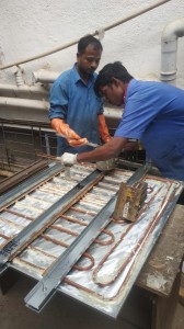 Two technicians applying thermal paste over evaporator coils in the workshop