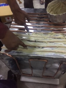 Technician troweling thermal paste over copper coils on a metal sheet
